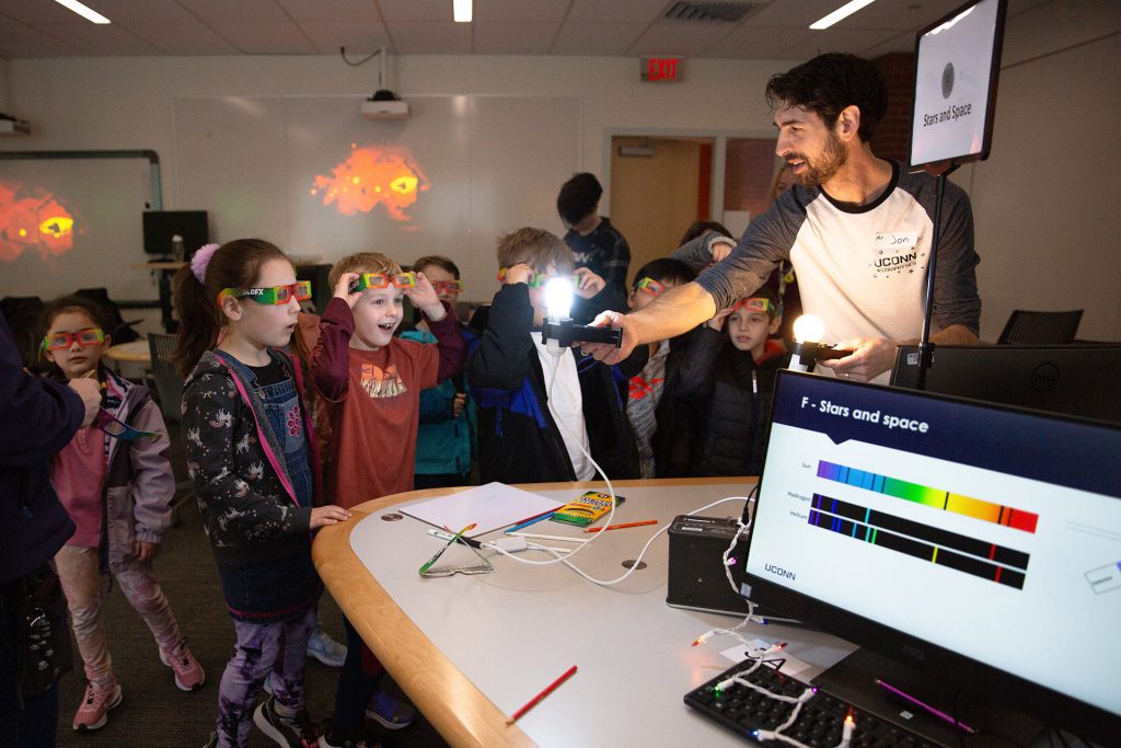 A professor shines a light during a science education class as visiting students watch with curiosity and amazement.